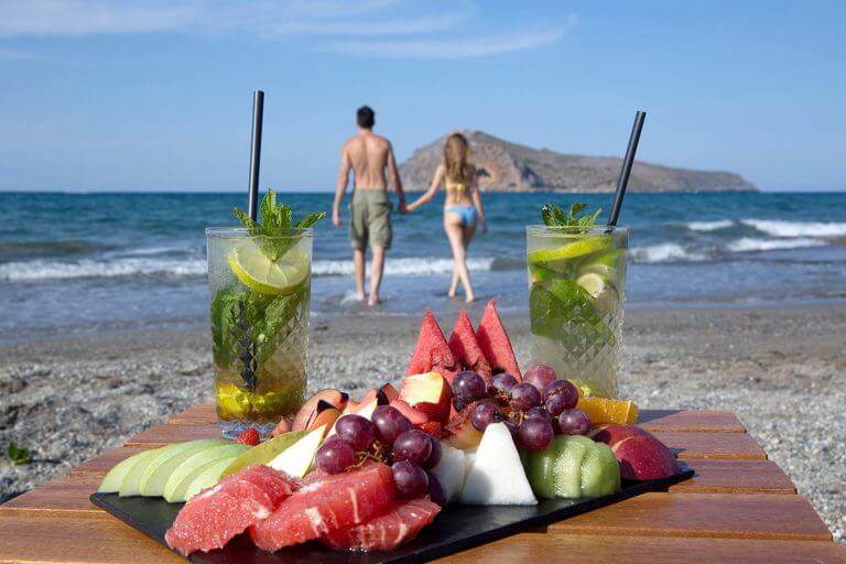 Couple walking along the seaside leaving drinks and fruit on table