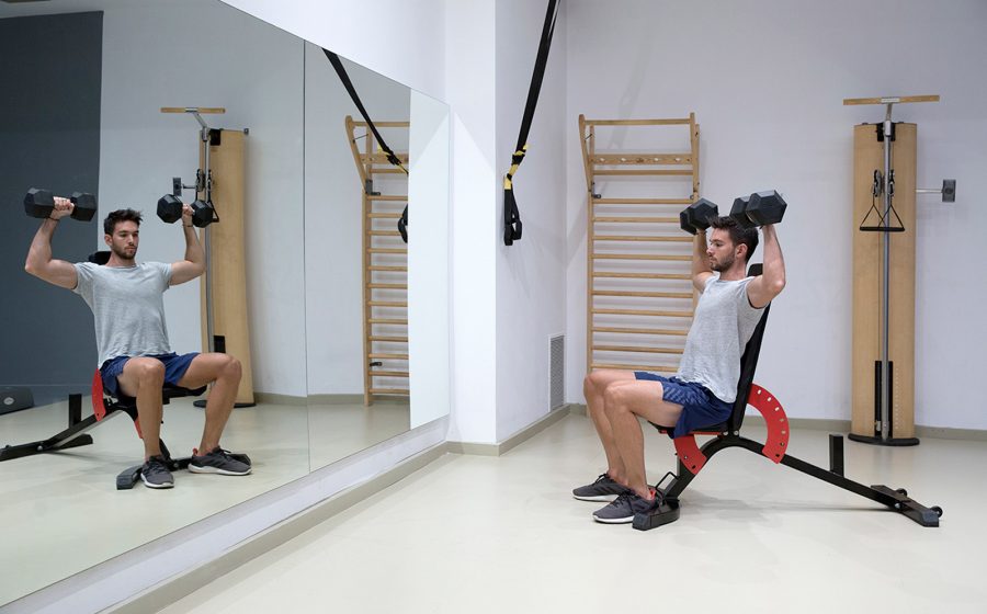 man pressing dumbbells looking at mirror